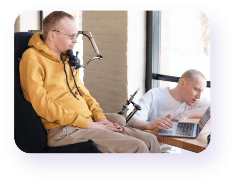 A man in a wheelchair with another man looking at a laptop